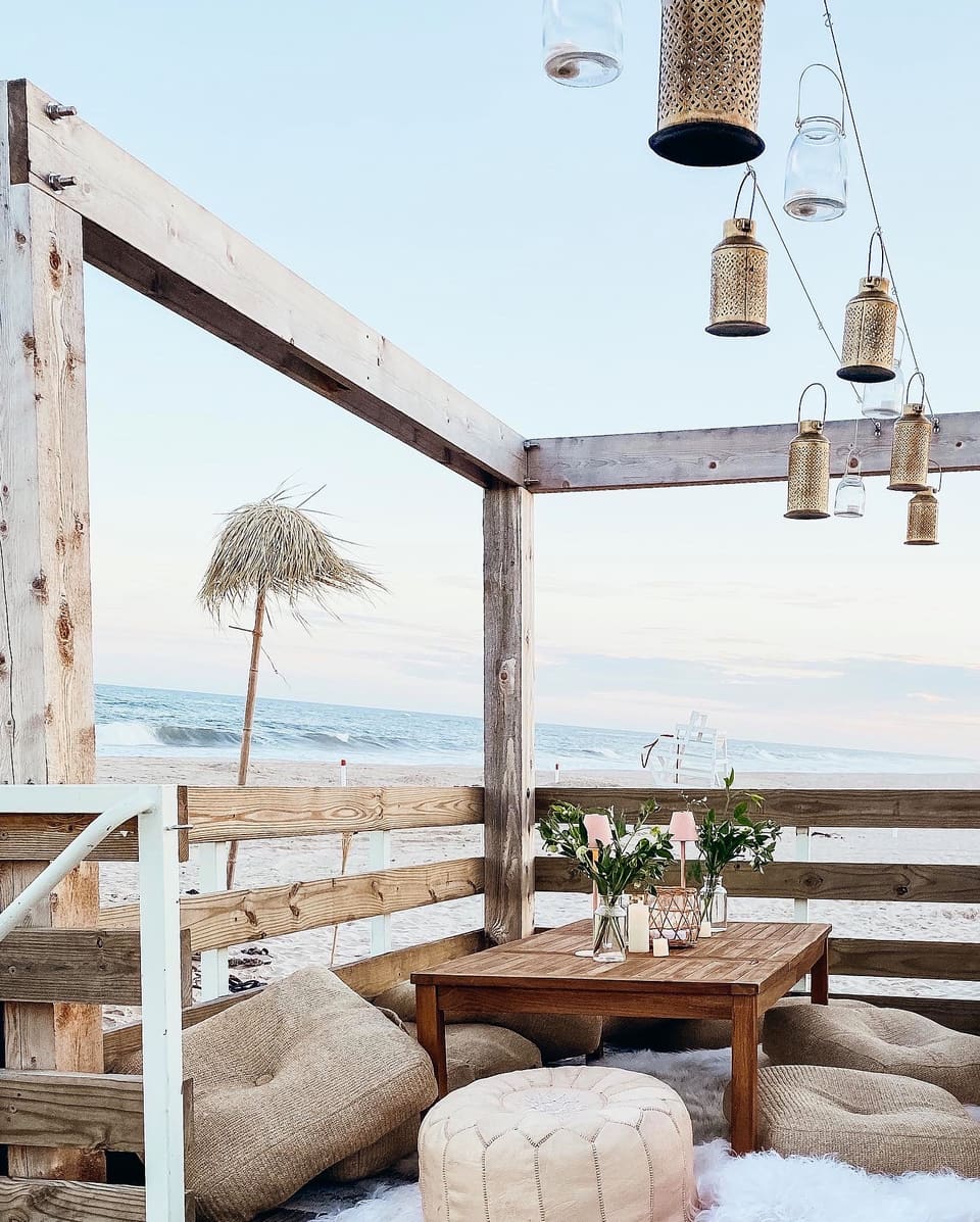 A beachfront pergola lounge at dusk, lanterns lit, the ocean behind